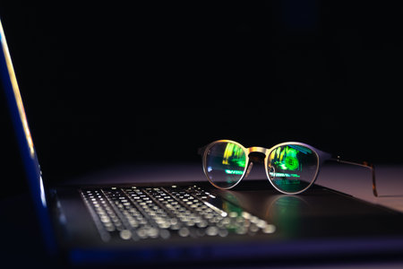 Reflection from a laptop in glasses on a dark background.
