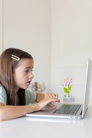 A schoolgirl studies online at home. The girl is typing on the laptop keyboard.の写真素材