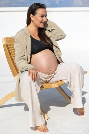 Stylish pregnant woman on a beautiful wicker chair. On a light background.の写真素材