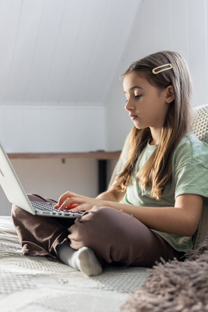 A schoolgirl studies online at home. The girl is typing on the laptop keyboard.