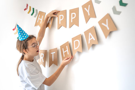A girl hangs a happy birthday sign on the wall. Birthday concept.の写真素材