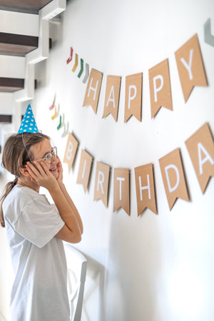 A girl hangs a happy birthday sign on the wall. Birthday concept.の写真素材