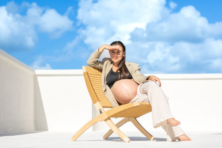 Stylish pregnant woman on a beautiful wicker chair. On a light background.の写真素材