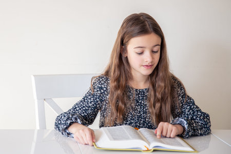 Happy girl reading a book at home. The girl is preparing for lessons at school