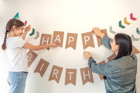 A mother with a child hangs a happy birthday sign on the wall. Birthday concept.の写真素材