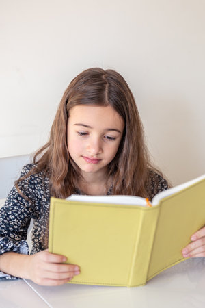 Sad girl reading a book at home. Girl student teaches lessons to school.の写真素材