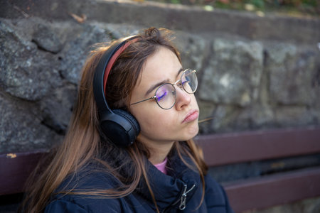 A serious girl in headphones sits on a bench. Emotions concept.の写真素材