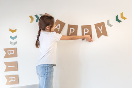Preparation for the birthday. Girl hangs Happy Birthday sign on a wall.の写真素材