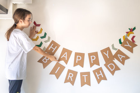 A girl hangs a happy birthday sign on the wall. Birthday concept.の写真素材