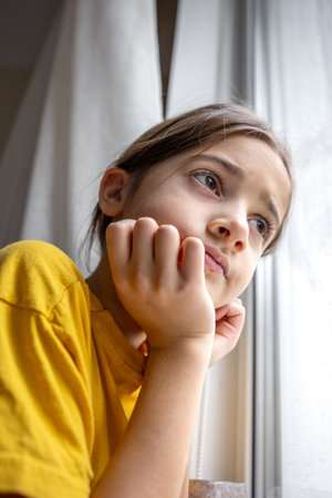 A gloomy and sad girl looks out the window. Emotions concept.の写真素材