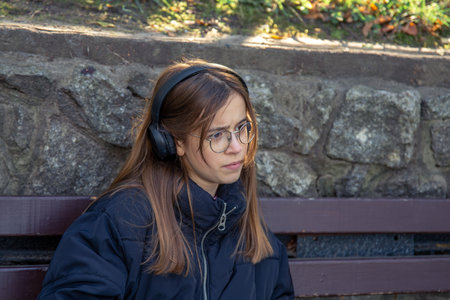A serious girl in headphones sits on a bench. Emotions concept.の写真素材