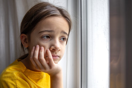A gloomy and sad girl looks out the window. Emotions concept.