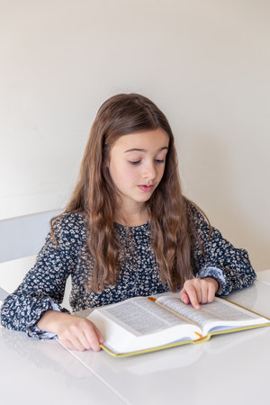 Happy girl reading a book at home. The girl is preparing for lessons at schoolの写真素材