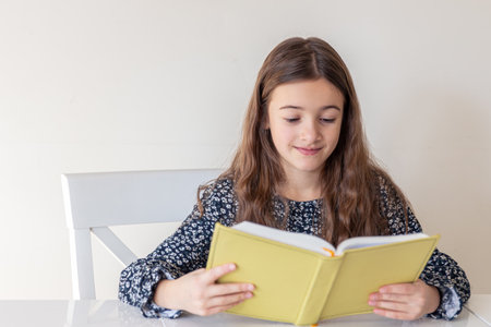 Happy girl reading a book at home. The girl is preparing for lessons at schoolの写真素材