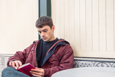 A young man reads a book in a coffee shop. Reading a book outdoors.の写真素材