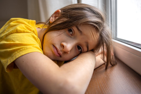 A gloomy and sad girl looks out the window. Emotions concept.の写真素材