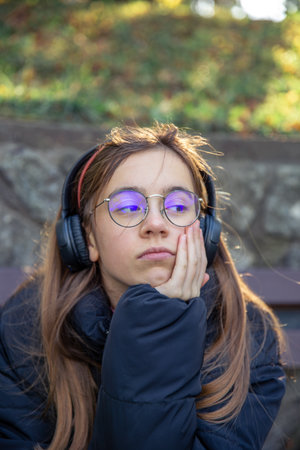 A serious girl in headphones sits on a bench. Emotions concept.の写真素材