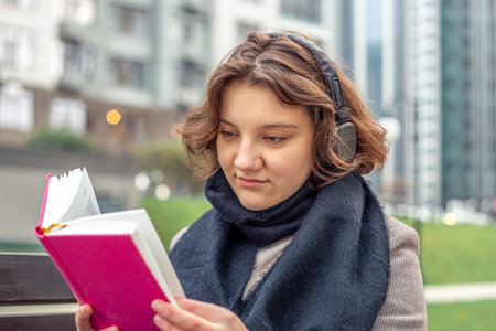Girl reading a book in the city. Girl reading a book and listening to music.の写真素材
