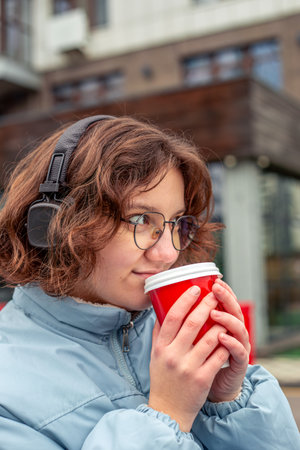 Young woman drinking coffee in the city and listening to music on headphones.の写真素材