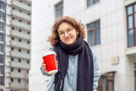 Student girl with coffee in her hands in the city. Looking at the camera.の写真素材