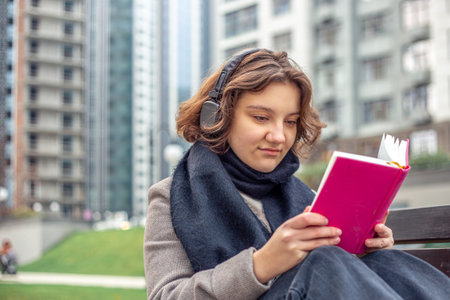Girl reading a book in the city. Girl reading a book and listening to music.の写真素材
