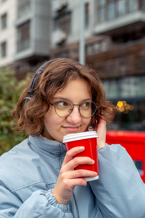 Young woman drinking coffee in the city and listening to music on headphones.の写真素材