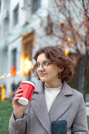 A young female student walks through the city with a coffee in her hands.の写真素材