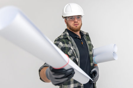 Male builder. Engineer in overalls and helmet holds blueprints and projects in his hands.