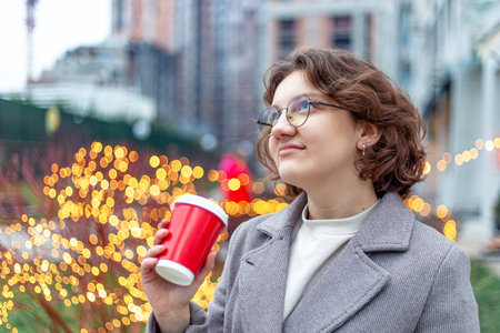 A young female student walks through the city with a coffee in her hands.の写真素材
