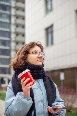 A young female student walks through the city with a coffee in her hands.の写真素材