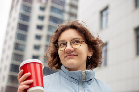 A young female student walks through the city with a coffee in her hands.の写真素材