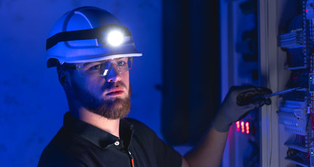 A male electrician works in a switchboard in overalls against the backdrop of emergency lighting.の写真素材