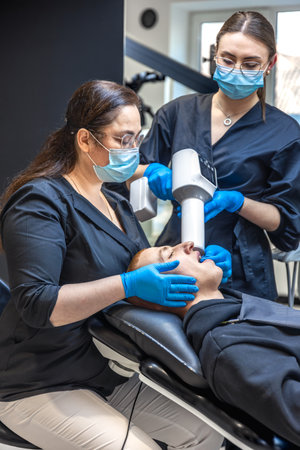 A team of dentists treats a patients teeth using modern equipment. Dentistry concept.の写真素材