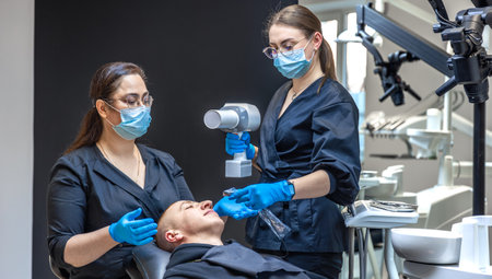 A team of dentists treats a patients teeth using modern equipment. Dentistry concept.の写真素材