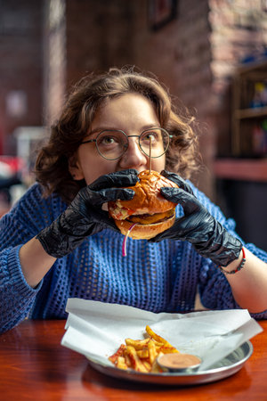 Young woman eating burger. Fast food. Cheat Meal. A woman in a burger restaurant.の写真素材