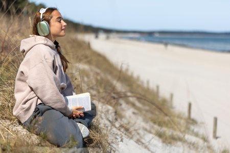 Teenage girl reading a book on the seashore. Girl listening to music on the seashore.の写真素材