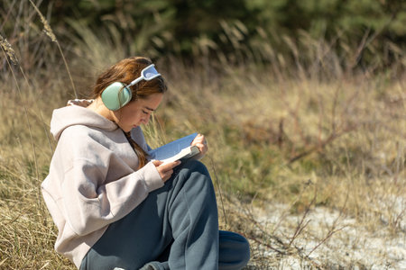 Teenage girl reading a book outdoors. Reading a book and listening to music.の写真素材