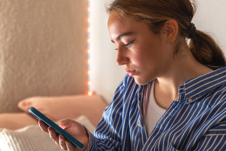 Teenage girl with phone in bed in the morning. Gadget addiction. Adolescence.の写真素材