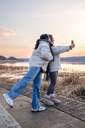 Walk along the promenade. A walk by the sea. Women taking photos at sunset.の写真素材