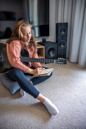 Teenage girl learning to play guitar at home. Girl composing music. Guitar.の写真素材