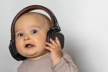 Baby with large headphones. Curious expression. Modern lifestyle