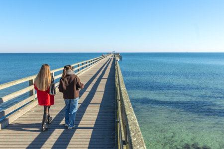 Two women on the pier. Rear view of two women walking along the pier. Sea.