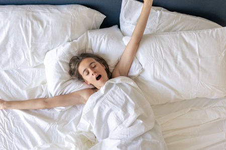 Sleepy morning yawn. Wide stretch. White bedding
