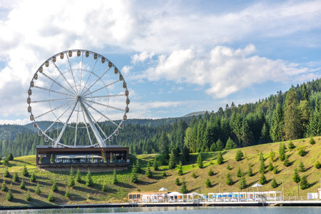 Ferris wheel above lake and green slopes. Summer resort by the water.の写真素材
