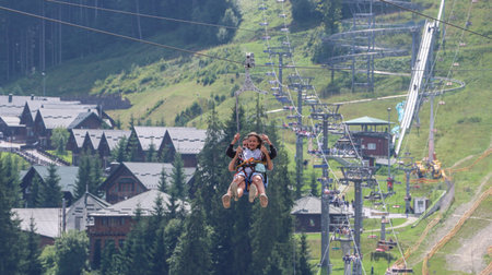 Girl riding a zipline above a mountain resort. Family adventure.の写真素材