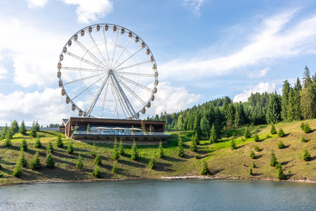 Ferris wheel above lake and green mountain slopes on a sunny day. Mountain attraction.の写真素材