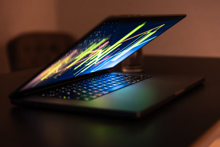 Half closed laptop with neon chart on desk. Night shift.