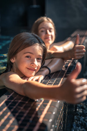 Two girls by the pool edge, thumbs up in frame. Summer relax.の写真素材
