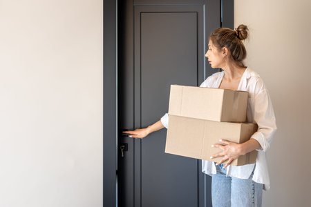 Young woman with boxes opens door with key. One person, new home.