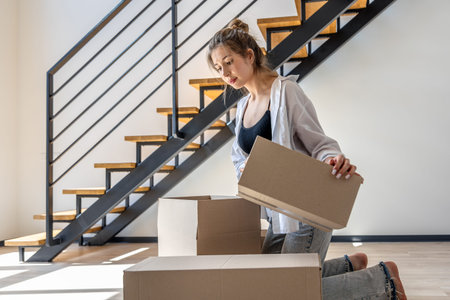 Woman by staircase sorting boxes, moving day. Focus and calm.